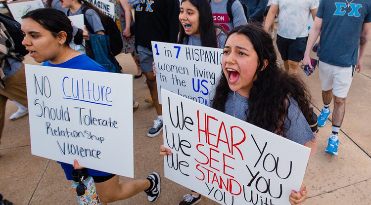 students walking in a protest holding signs and yelling