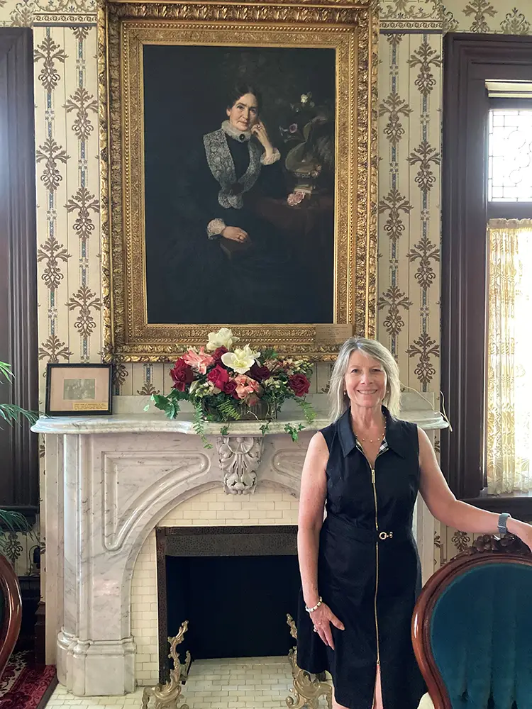 Mary Morgan in Breezedale, 2021. The portrait behind her is of Sarah Cook Stansbury Sutton, the mansion’s original owner (with husband James).