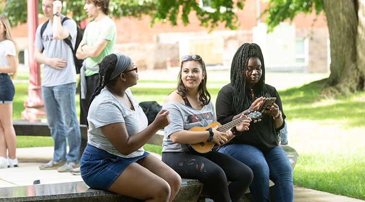 Three students sitting on a bench outdoors