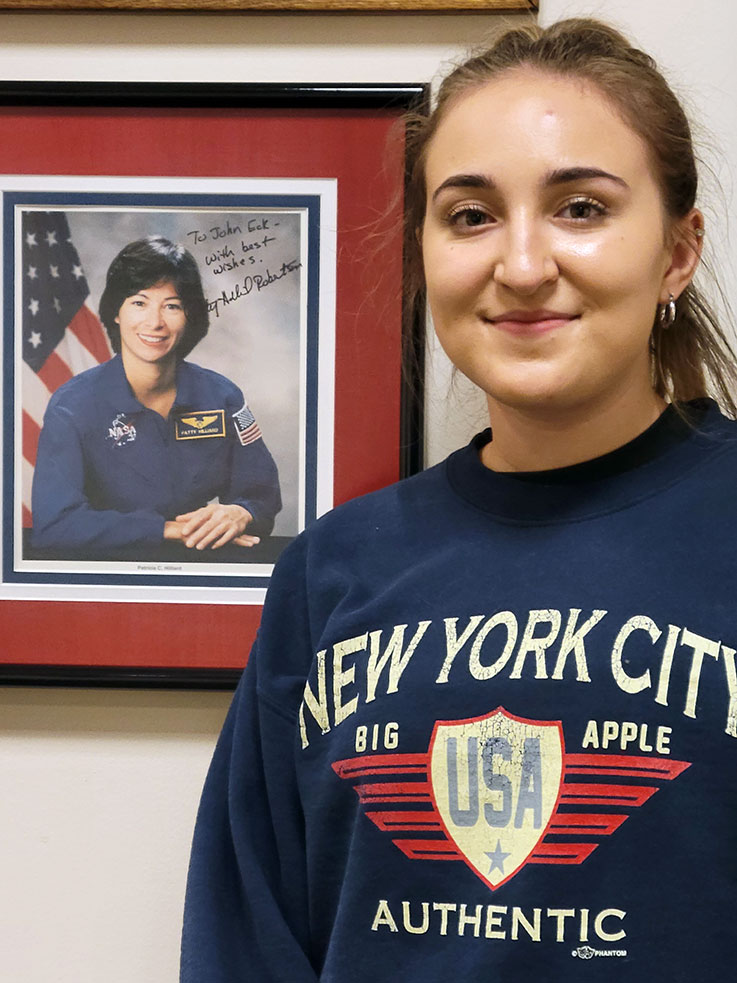 Scholarship recipient Kendra Bass in front of the plaque honoring the late Patricia Hilliard Robertson, located in the John J. and Char Kopchick College of Natural Sciences and Mathematics Dean’s Office.