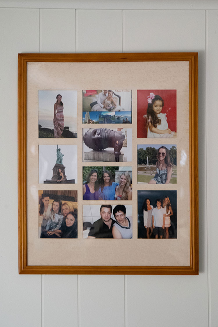 A collage picture frame in light brown, with 10 photos of various people, hangs near the top of a white wall. 