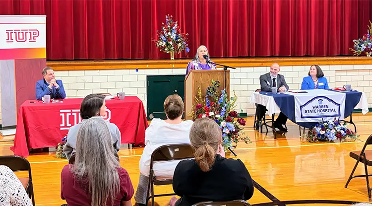 Dr. Miko Rose speaking at a podium surrounded by representatives from IUP and Warren State Hospital
