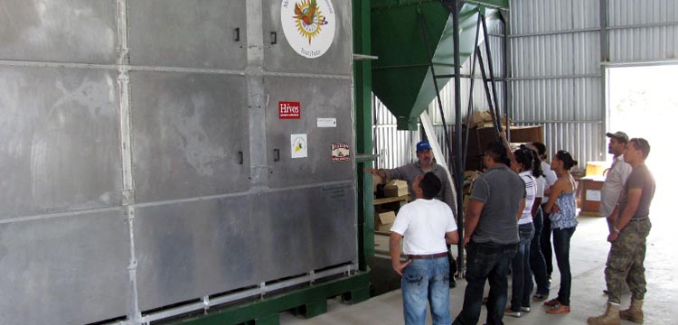 Workers being instructed in front of a metal coffee bean dryer