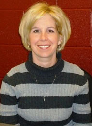 Head-and-shoulders photograph of Kristy Chunta in front of a red wall and wearing a sweater with wide black and gray horizontal stripes.