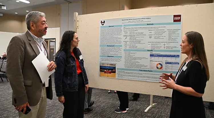 IUP proposed college of osteopathic medicine Associate Founding Dean Dr. Luke Mortensen, left, talks with Dr. Jodie Seybold, Department of Allied Health, far right, who received the overall best poster award for her research poster, “Rural Family Kitchen Empowerment (RFKE) Initiative.”