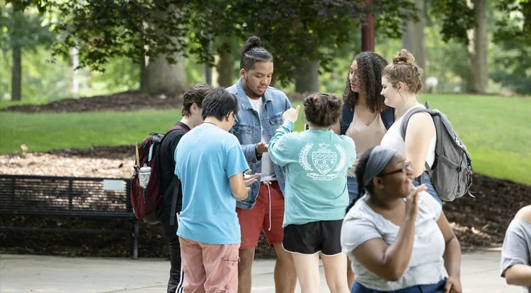 A group of six students talk outside while standing in a circle