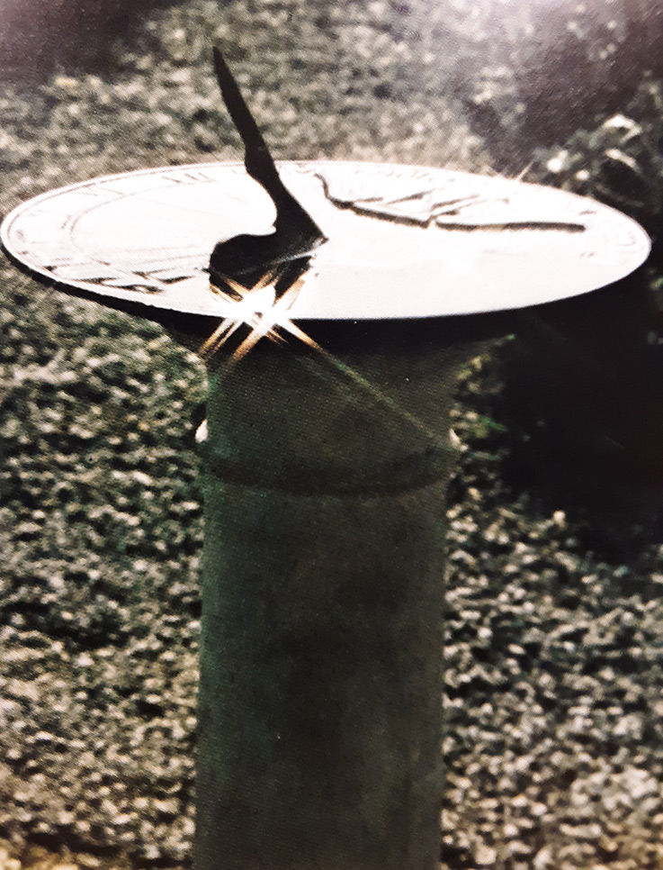 Light reflects off a sundial sitting in a garden-type setting