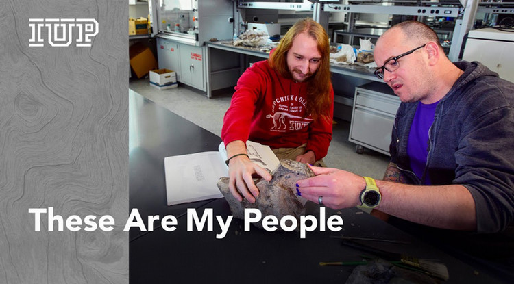 Two people examining a fossil on a lab table.  The words Thes Are My People are on the bottom left.  The IUP logo is at the top left.