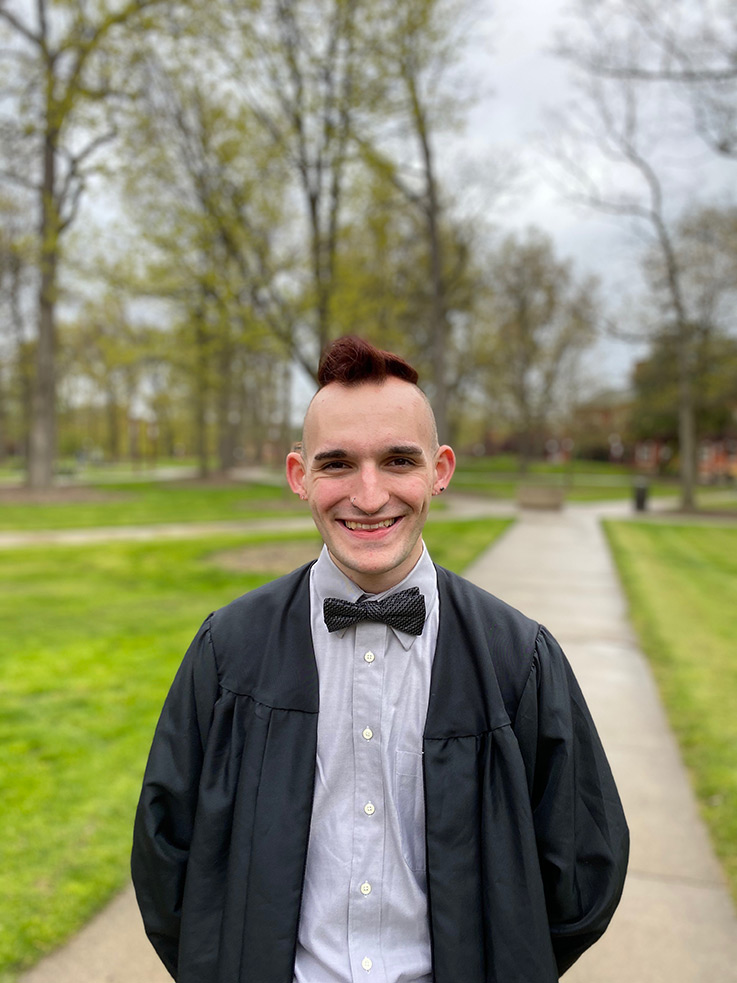 Outdoor portrait of Austin Marsico wearing a graduation gown in IUP’s Oak Grove