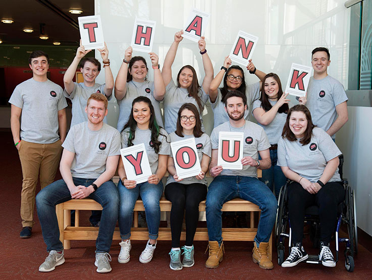 Twelve IUP students smiling at the camera and holding up large alphabet letters that spell THANK YOU