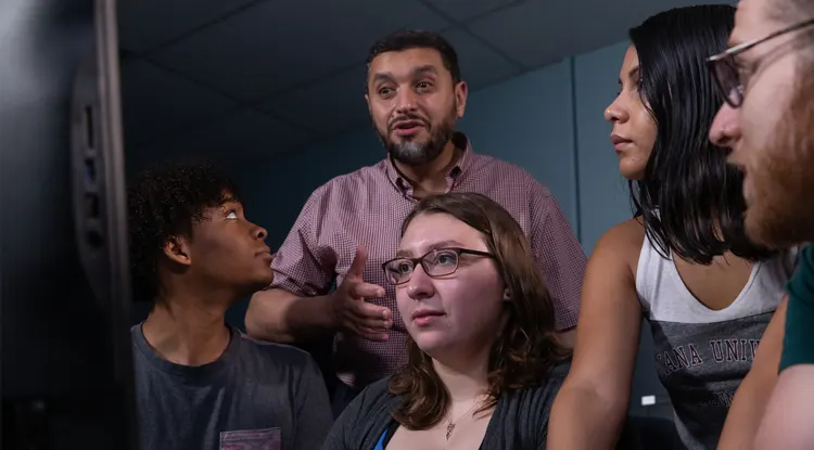 a professor standing and speaking over the shoulders of sitting students