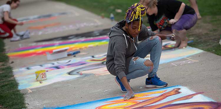 Students chalking the sidewalk in the Oak Grove, a campus tradition