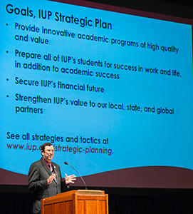 President Driscoll gives his speech before a screen highlighting four Strategic Plan points