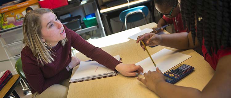 A young teacher sits to explain a math problem to students.