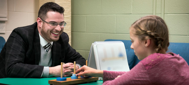 An IUP student talks to a child while seated with her at a table