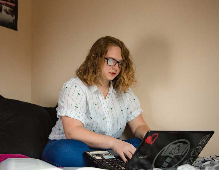A student sitting on a bed working on a laptop computer