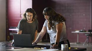 two people standing behind a laptop while viewing the screen