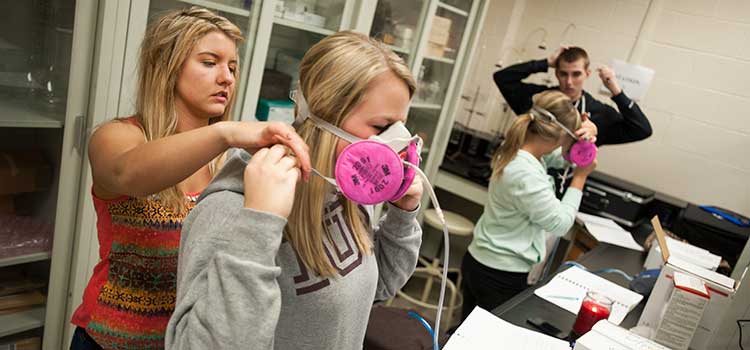 Students helping other students put on air filtration devices 