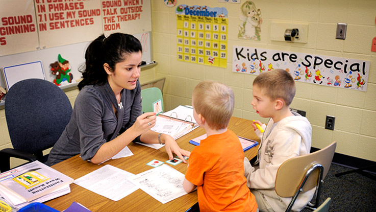 A student teacher works with two young students on speech exercises.