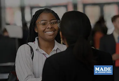 An over the should photo of two people facing each other and smiling.  The Made in Johnstown logo is on the bottom right.