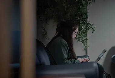 A side view image of a person sitting in a black chair working on their laptop.