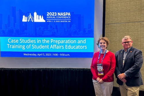 Dr. John Wesley Lowery and Dr. Mimi Benjamin in front of banner that reads 2023 NASPA Annual Conference. 