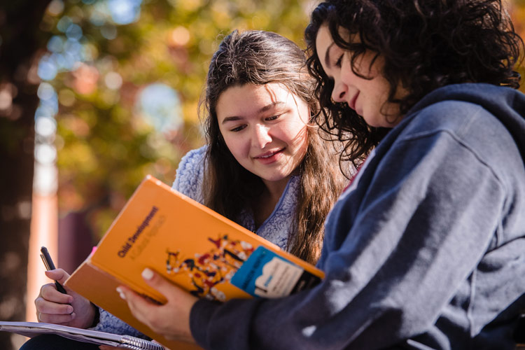 Two students sitting and studying a book in the autumn oak grove" class="float-left one-third-width-image
