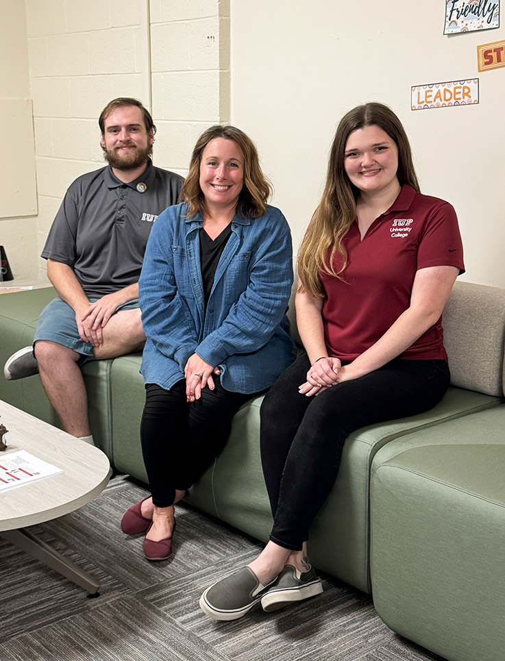 Three people, a man and two women, sit on a green vinyl couch in the newly updated waiting area of the Advising Center.