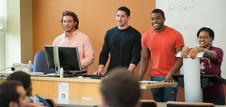 Four students give a presentation at the front of a classroom