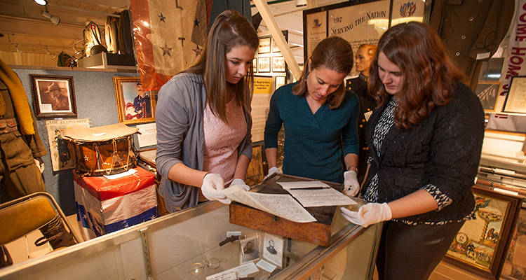 Three history students wearing gloves exam documents in a museum