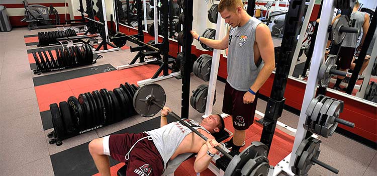 A student watches another another bench press weights.