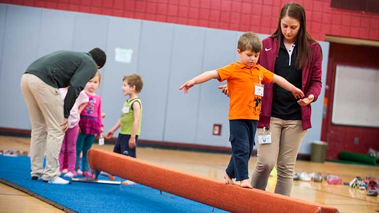 Kinesiology student helping child across balance beam