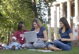 Three students doing school work in the Oak Grove outside of Waller Hall