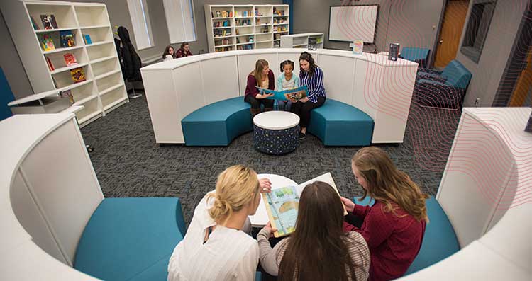 Two student teachers sit on a bench with a younger child reading a book in the Literacy Center.