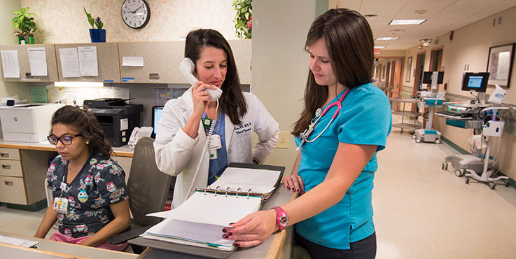 Nursing students in a hospital nurse's station look over records